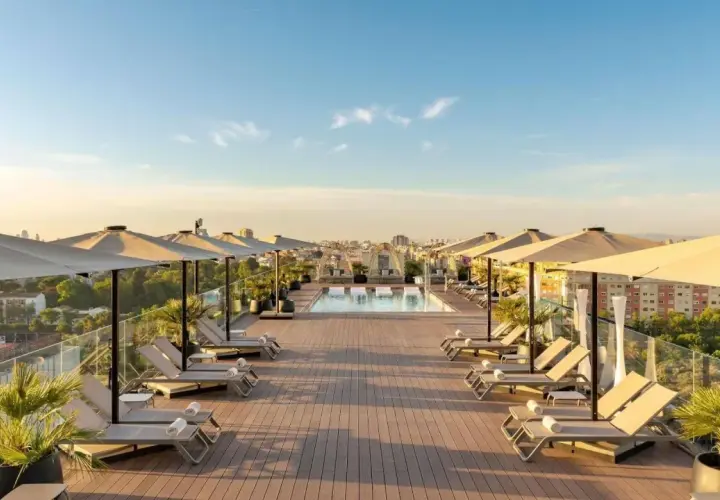 Terraza con piscina y tumbonas en el Novotel Valencia, vistas a la ciudad al atardecer.