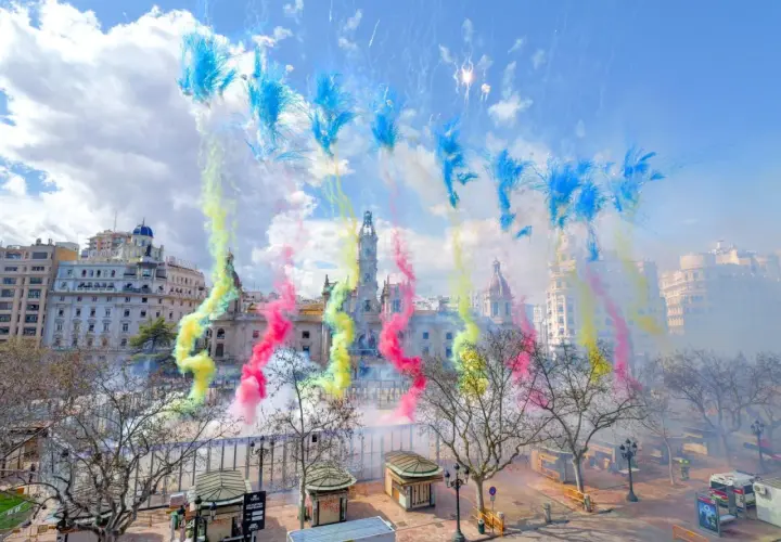 Explosión de color y ruido en la mascletà hoy. El cielo se tiñe de azul, amarillo y rosa sobre edificios históricos.
