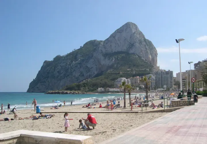 Gente disfrutando del sol y el mar en la playa de la Fossa, con el imponente peñón de Ifach de fondo.