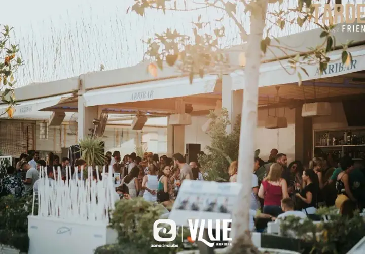 Gente disfrutando en Arribar, un lugar con ambiente de fiesta. El logo de @VLUE destaca.