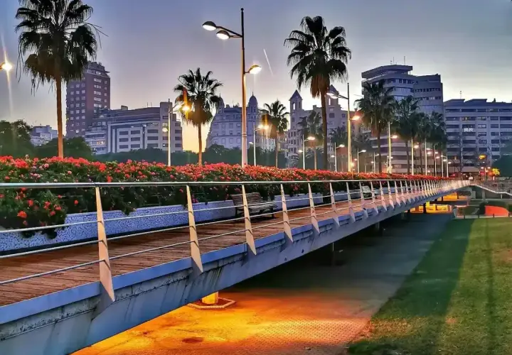 Puente iluminado con palmeras y flores rojas en la ciutat vella valencia al atardecer.