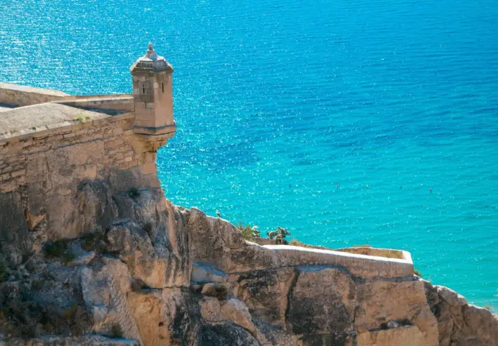 Torreón en el Castillo de Santa Bárbara, con el mar turquesa de fondo. Una vista icónica de la exposición alicantina.