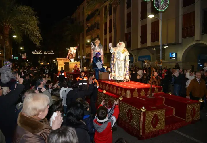 La cabalgata de Reyes en Valencia ilumina la noche con sus majestuosas carrozas y la multitud expectante. Melchor, Gaspar y Baltasar saludan a los niños.