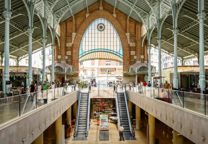Interior del Mercado de Colón, con sus arcos de hierro y cristal, escaleras mecánicas y puestos de comida.