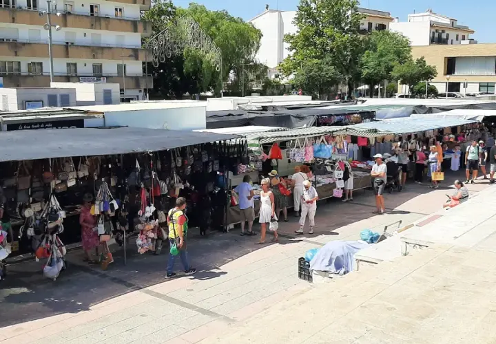 Gente paseando y comprando en el mercadillo de Jávea, con puestos de bolsos y ropa bajo toldos.