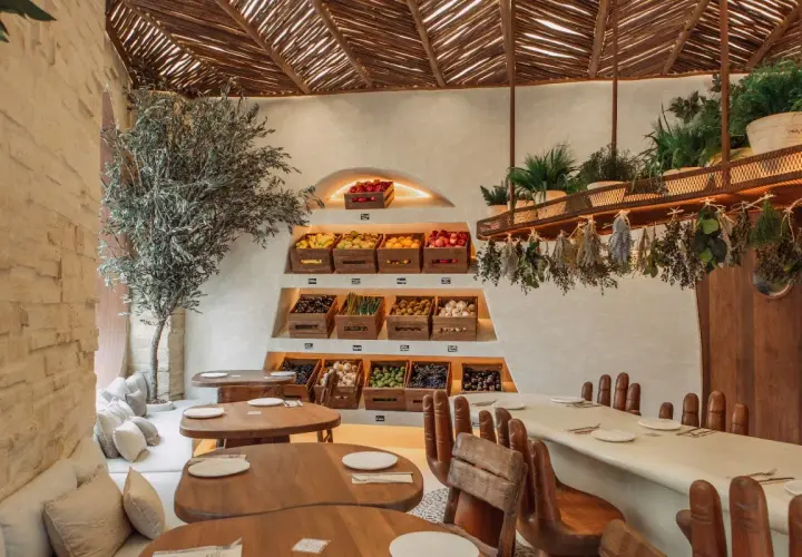 Interior de restaurantes en Valencia con encanto, con estanterías de frutas y verduras frescas, un olivo y mesas de madera.