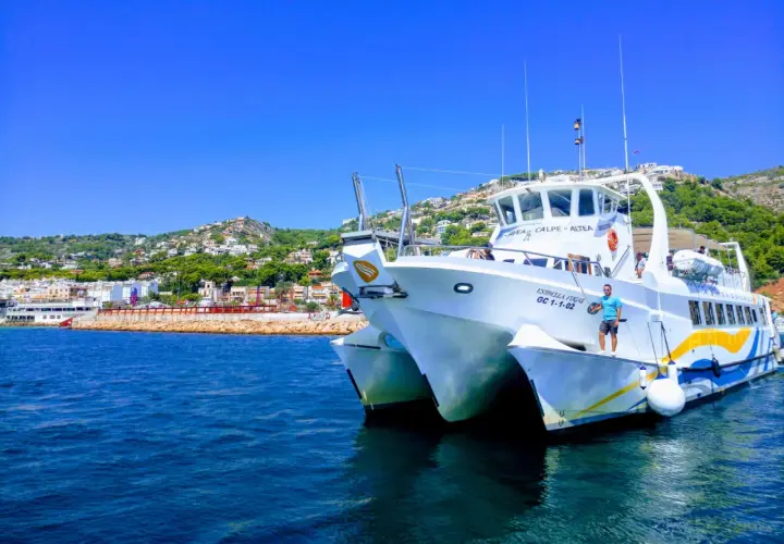 Catamarán "Estrella Fugaz" en el puerto de Dénia, con la costa y el monte al fondo.