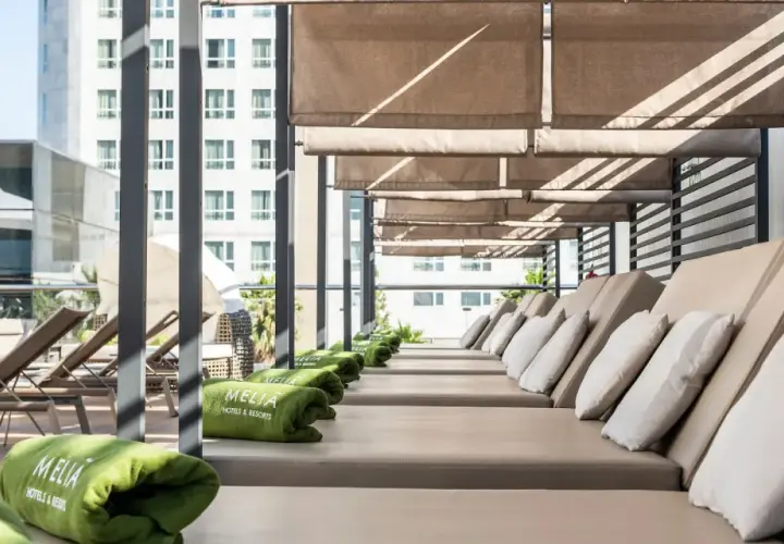 Tumbonas listas para el relax en la terraza del Meliá Valencia, con toallas verdes y vistas a la ciudad.