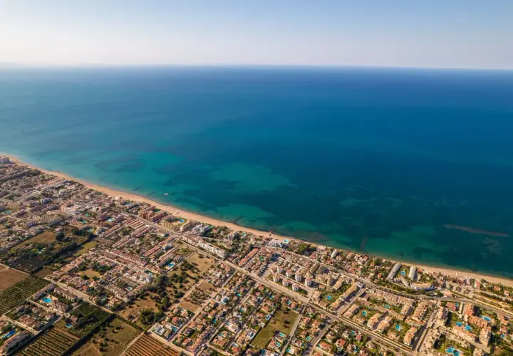 Vista aérea de la playa de arena de Dénia, con el mar azul turquesa y edificios residenciales.