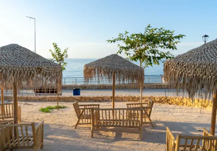 Mesas de madera y sombrillas de paja en la cala Lanuza, listas para disfrutar del mar y el sol.