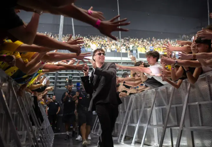 Quevedo saluda a sus fans en un concierto, con manos extendidas y móviles grabando el momento.