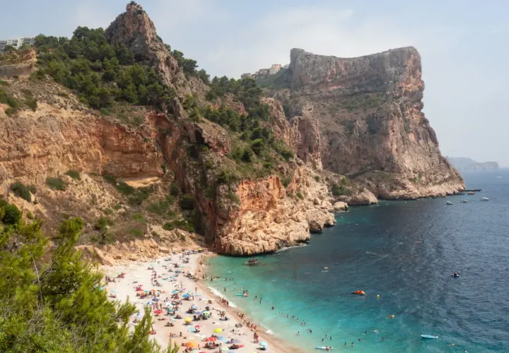 Una cala rocosa con aguas turquesas, gente disfrutando del sol y el mar. Un paraíso entre las mejores playas de la Costa Blanca.