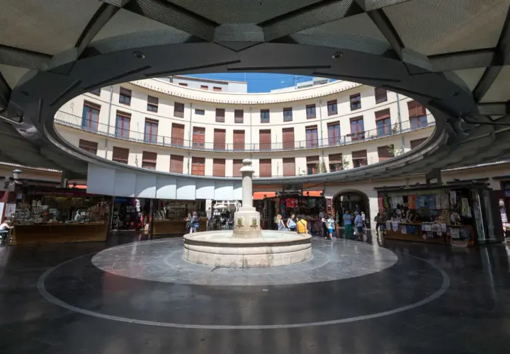 Fuente central en la plaza redonda valencia, rodeada de edificios curvos y puestos de venta.