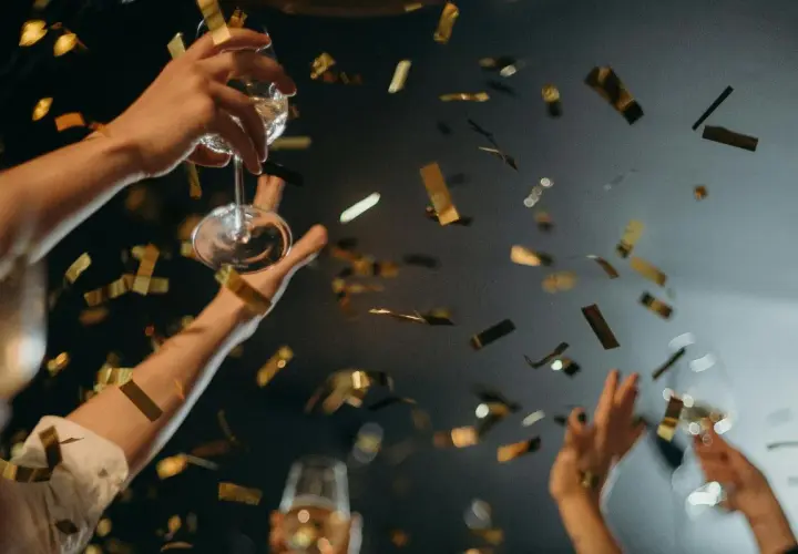 Manos brindando con copas y confeti dorado cayendo. ¡Una celebración perfecta para saber qué hacer en Nochevieja en Valencia!