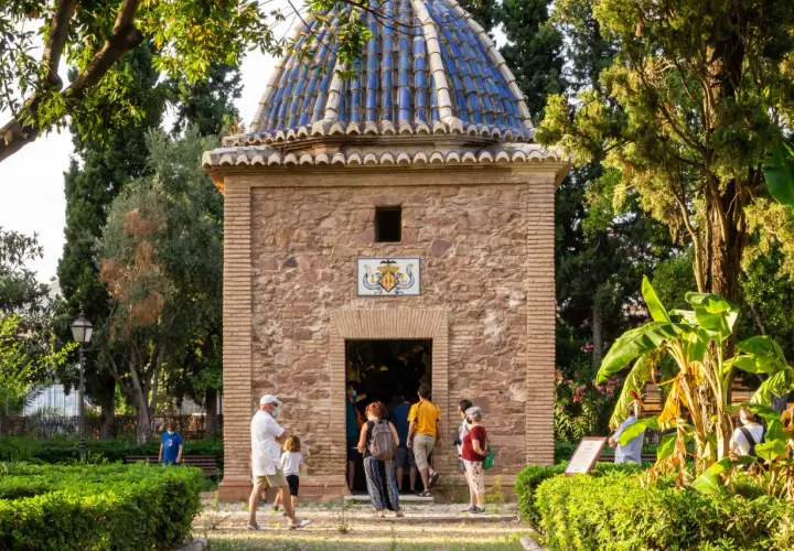 La ermita de Sant Jordi, con su cúpula azul y fachada de piedra, recibe a visitantes entre exuberante vegetación.