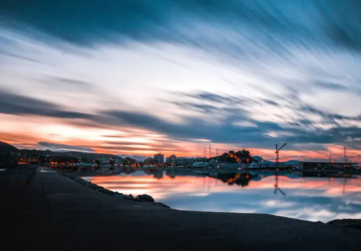 Atardecer en un puerto, con reflejos vibrantes en el agua. ¿Costa Blanca o Costa del Sol? La belleza es innegable.