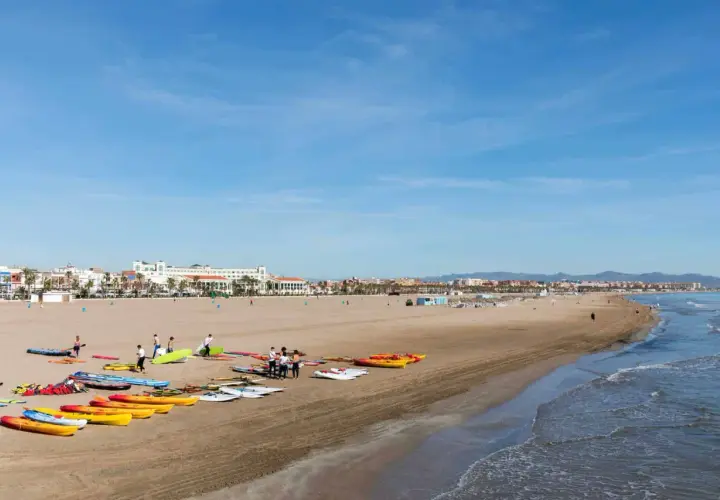 Gente prepara kayaks y tablas en la playa Malvarrosa, lista para un día de sol y mar.