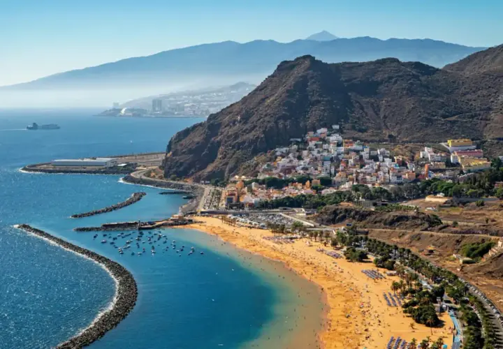 Vista aérea de una playa dorada y un pueblo costero con casas blancas y coloridas en la costa blanca España. Montañas y el mar azul completan la escena.
