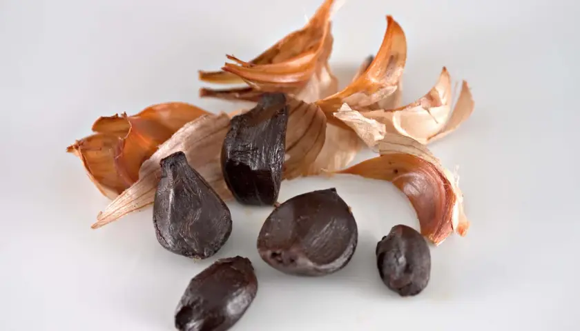 Dientes de ajo negro, con cáscaras secas de color naranja y blanco, evocan el sabor único del ajo negro alicante.