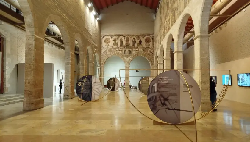 Exposición en el Almudín de Valencia, con arcos de piedra, murales antiguos y paneles circulares que narran la historia del Santo Cáliz.
