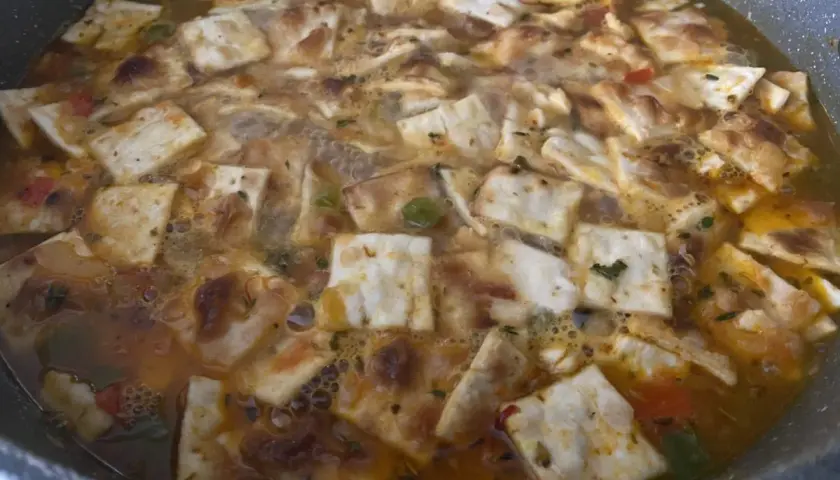 Gazpacho marinero alicantino burbujeante en una sartén, con trozos de pan tostado y verduras.