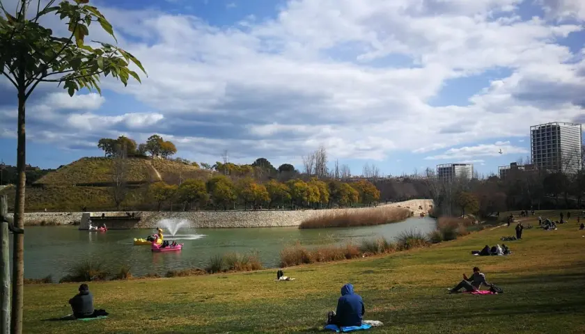 Gente relajándose en el césped del parque de cabecera, con un lago y barcas de pedales al fondo.