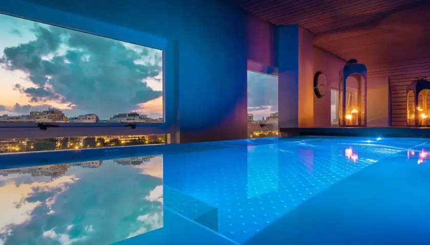 Piscina iluminada con luces azules en un spa de Valencia, con vistas a la ciudad al atardecer.