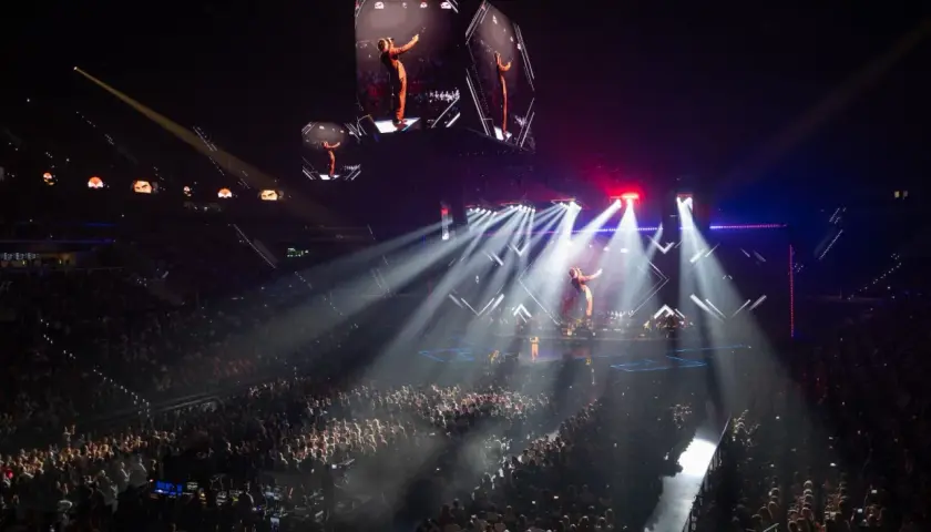 Un artista en un escenario iluminado por focos, con pantallas gigantes mostrando su imagen. ¡Imagina los conciertos Valencia 2026!