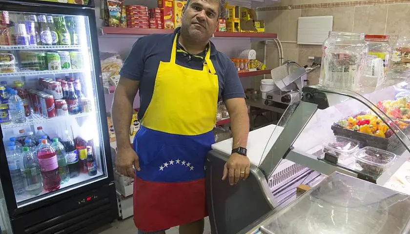 Hombre con delantal de Venezuela en el mercado de Torrefiel, rodeado de productos en neveras y estanterías.