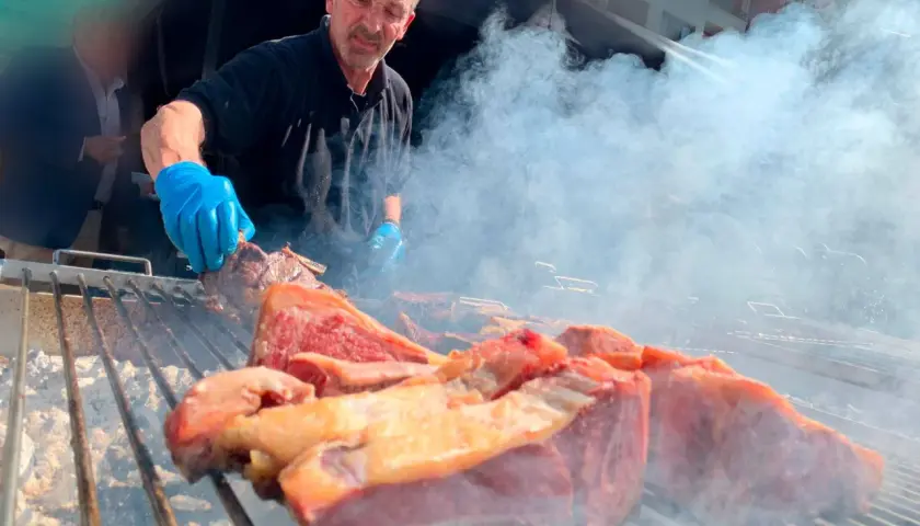 Hombre con guantes azules cocina carne en una parrilla humeante, un festín de carne en el **meat carnival Valencia**.