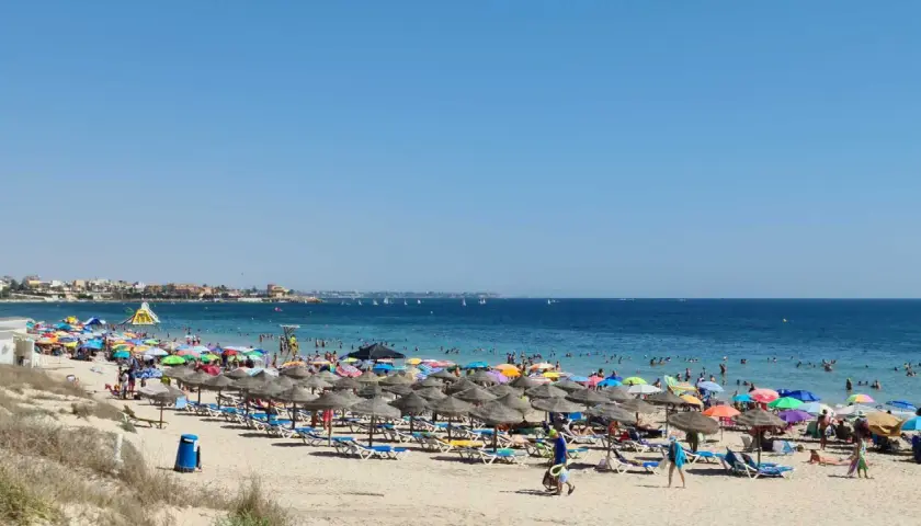Día soleado en la playa de las Higuericas, con mucha gente disfrutando del mar y la arena bajo coloridas sombrillas.
