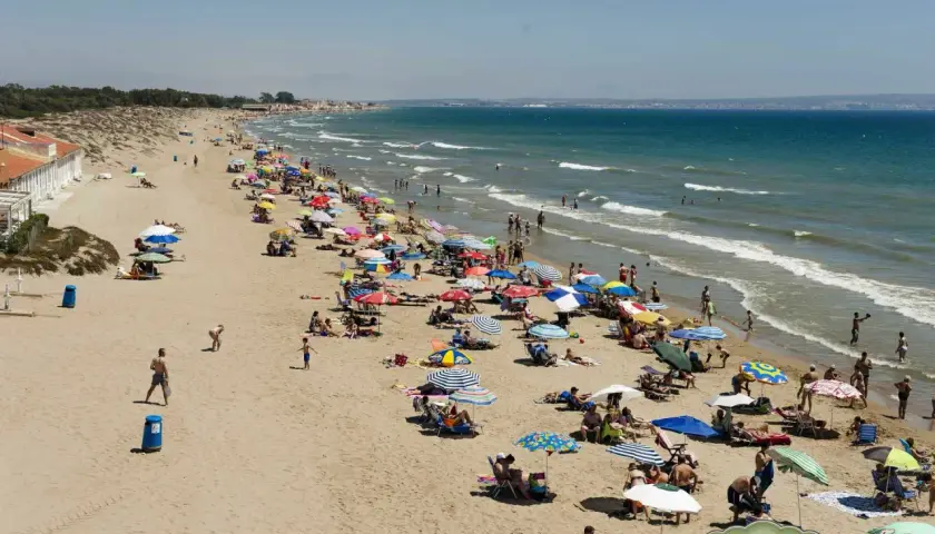 Gente disfrutando del sol y el mar en la playa la marina, con sombrillas de colores y aguas tranquilas.