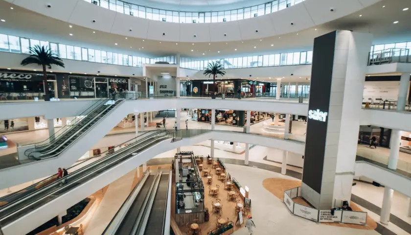 Interior de un moderno centro comercial en Valencia, con escaleras mecánicas, palmeras y tiendas. Un lugar ideal para ir de compras.