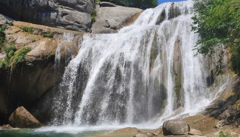 Cascada del Moli, con agua cayendo sobre rocas y vegetación exuberante, formando una piscina natural.