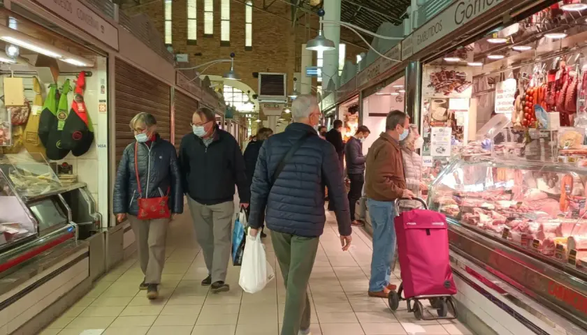Gente comprando en el mercat central d'Alacant, con puestos de embutidos y carnes.