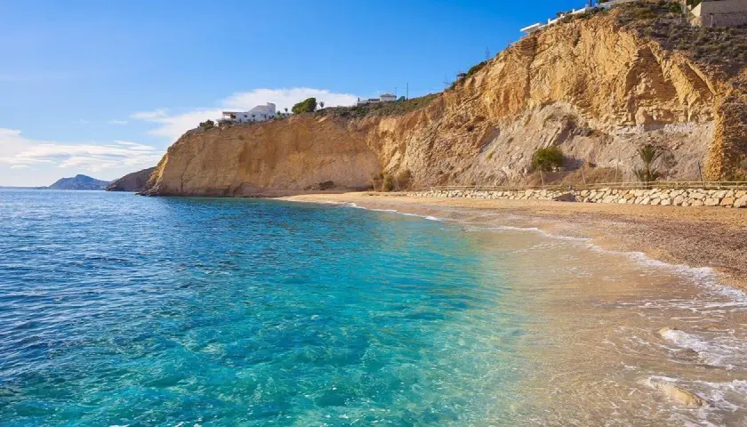 Aguas cristalinas y playas tranquilas en Alicante, con acantilados dorados y casas blancas en la cima.