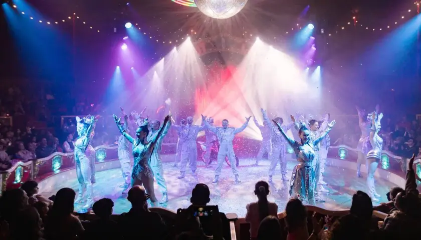 Artistas del circo Raluy en Alicante, bajo una bola de discoteca, con confeti cayendo y público aplaudiendo.