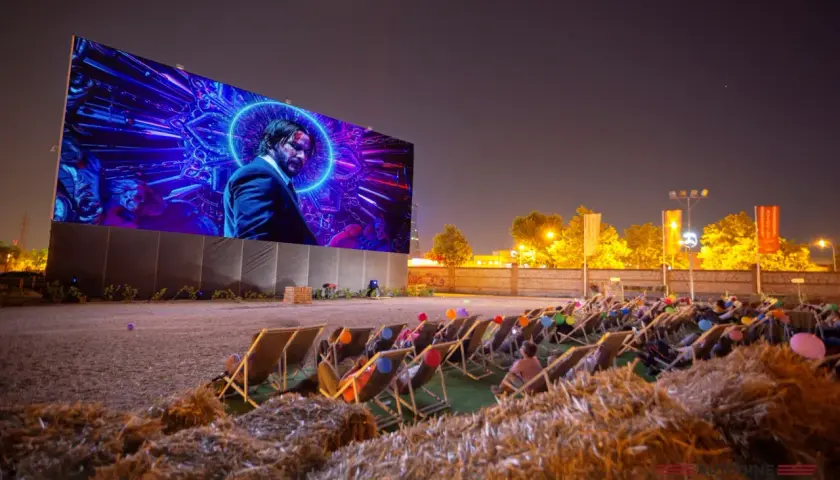 Noche de cine al aire libre en Valencia. Gente relajada en tumbonas viendo una película en pantalla gigante.