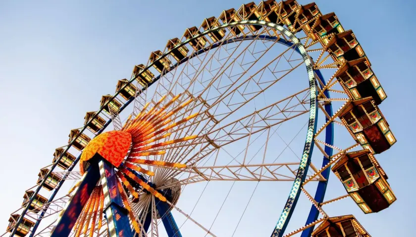 La noria iluminada, una de las atracciones principales de la feria de Valencia, se alza contra el cielo azul.
