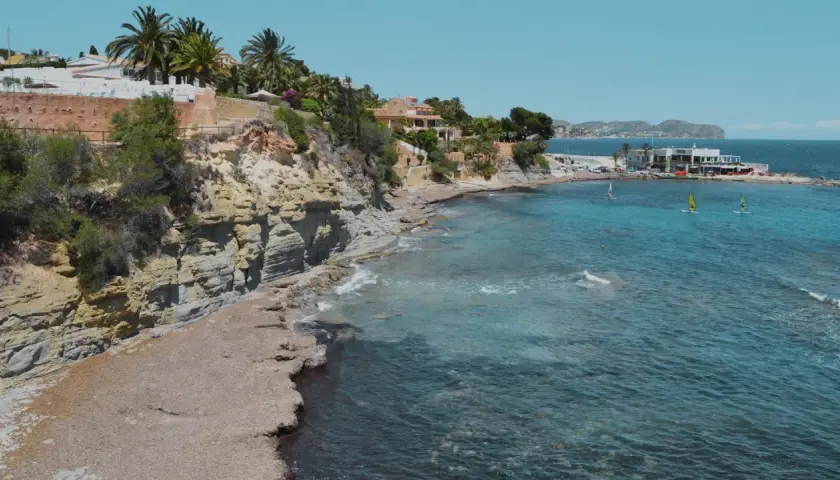 Acantilados y calas rocosas con aguas turquesas, perfectas para descubrir las playas cerca de Calpe. Windsurfistas disfrutan del mar.