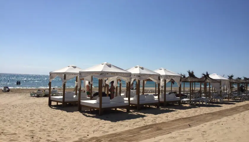 Días soleados en la playa Carabassi, con toldos blancos y camas de día listas para el relax junto al mar azul.