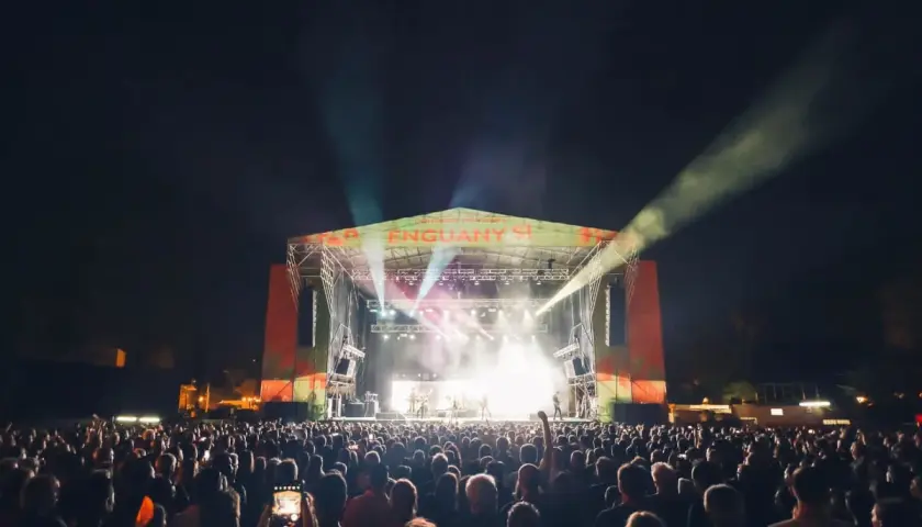 Multitud disfrutando de los **concerts de Vivers** bajo un cielo nocturno iluminado por focos y la energía de la banda en el escenario.