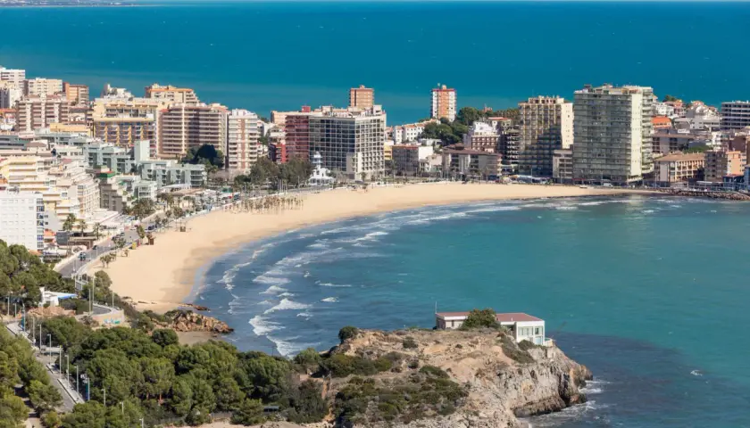 Vista panorámica de la **playa de la Concha Oropesa**, con edificios residenciales, el mar azul y una costa rocosa.
