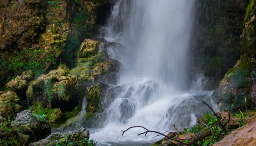 Cascada con rocas cubiertas de musgo y vegetación exuberante.