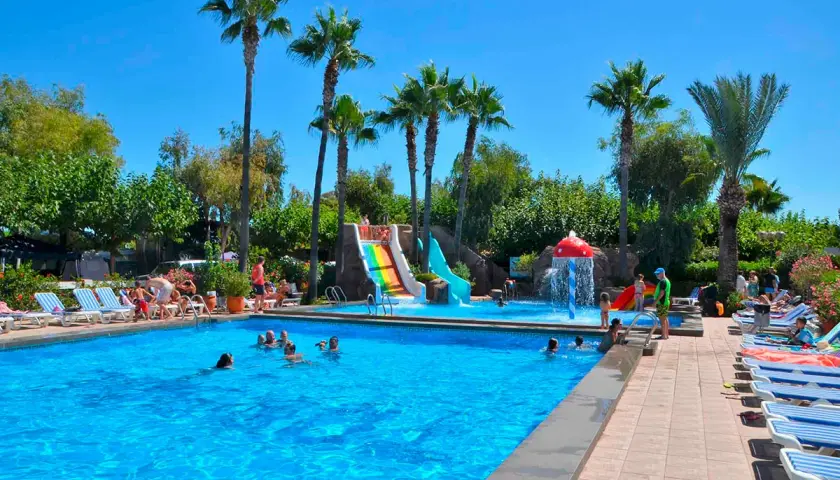 ¡Un día bravo en la playa! Niños y adultos disfrutan de toboganes acuáticos y una piscina refrescante bajo palmeras.