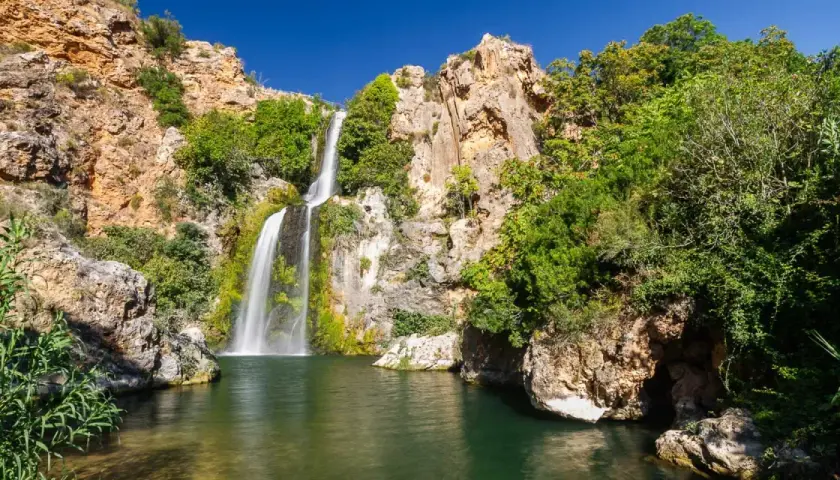El Salto de Chella, una cascada imponente rodeada de rocas y vegetación exuberante, cae en una poza de agua verde.