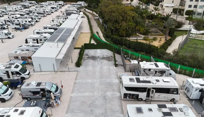 Amplio camper park en Alicante con numerosas autocaravanas y caravanas aparcadas, algunas con paneles solares.