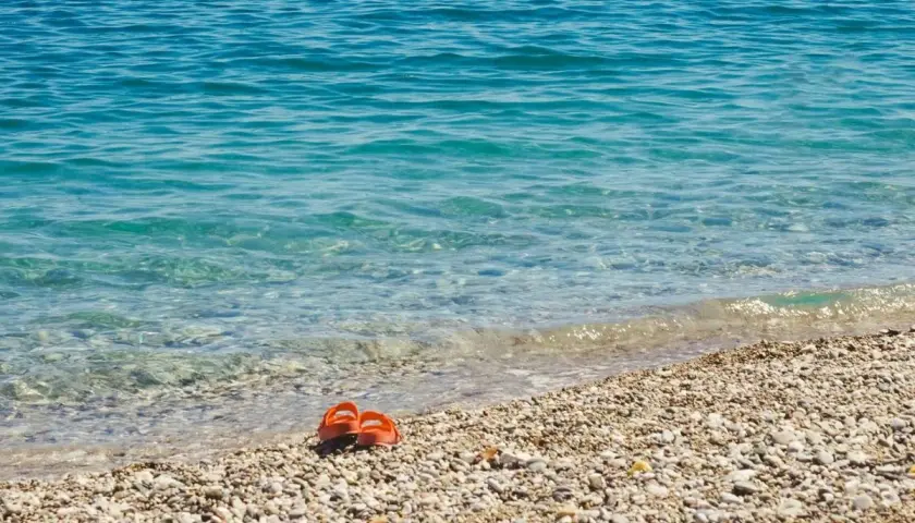 Chanclas naranjas abandonadas en la **playa Malvarrosa de Corinto**, esperando a su dueño junto a las aguas cristalinas.
