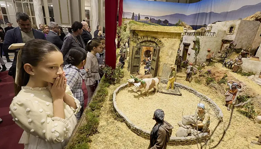 Niños observan un detallado belén en el Ayuntamiento de Valencia, con figuras que recrean la vida en un pueblo antiguo.