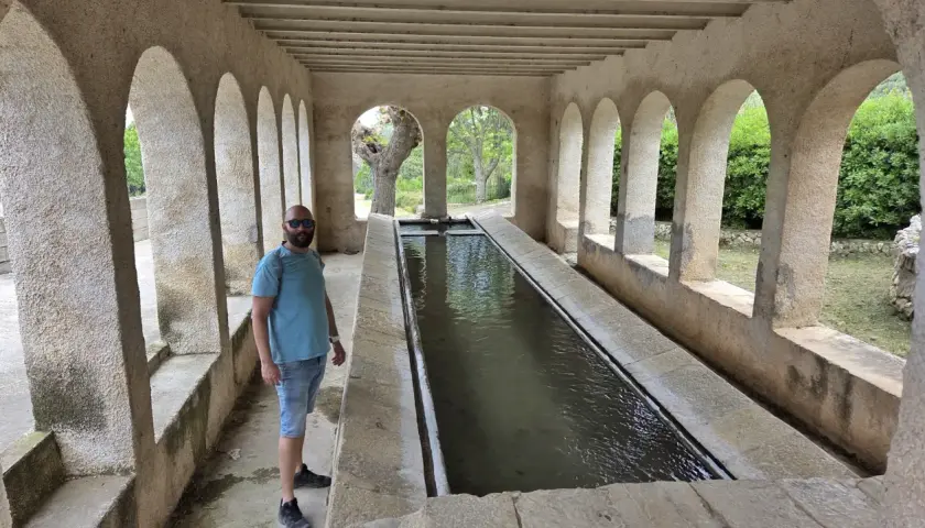 Un hombre posa junto a una larga pila de agua, un lugar que parece la "catedral del senderismo" por su arquitectura y entorno natural.